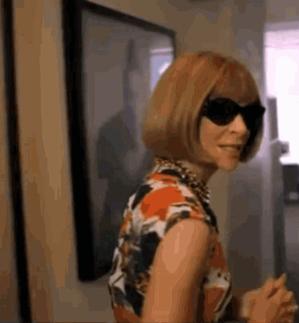 a woman wearing sunglasses and a floral dress smiles