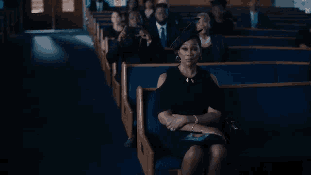 a woman in a black dress is sitting in a row of church pews