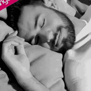 a man with a beard is sleeping with his eyes closed in a bed .