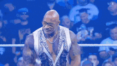 a bald man is standing in a wrestling ring with a crowd watching .
