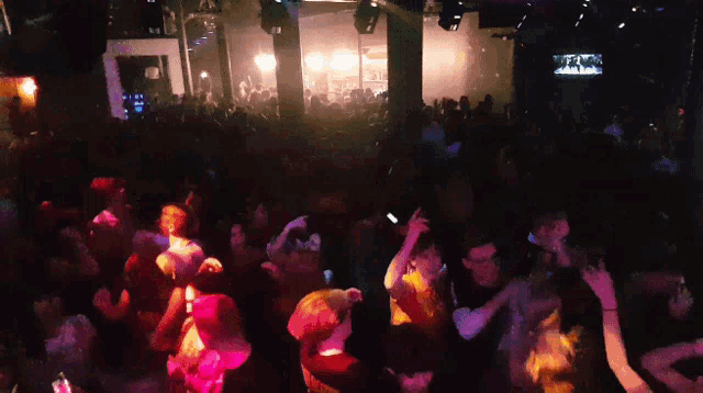 a crowd of people dancing in a dark room with purple lights