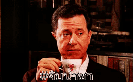 a man in a suit and tie is drinking from a teacup with a rose on it .