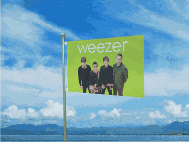 a weezer flag flies in the wind with mountains in the background