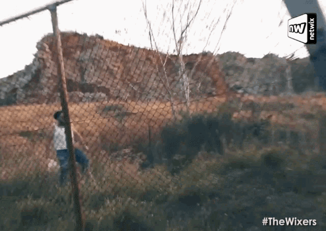 a person standing behind a chain link fence in a field with a mountain in the background .