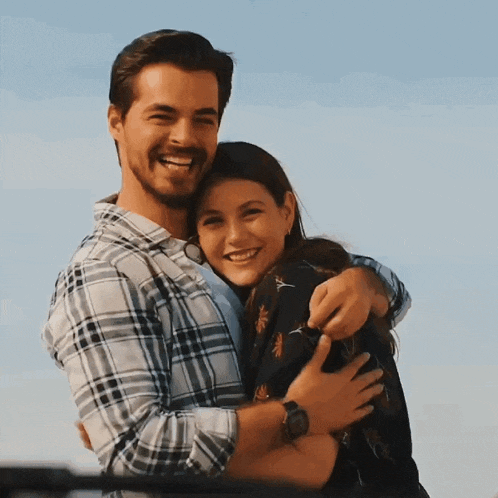 a man in a plaid shirt hugging a woman in a black dress
