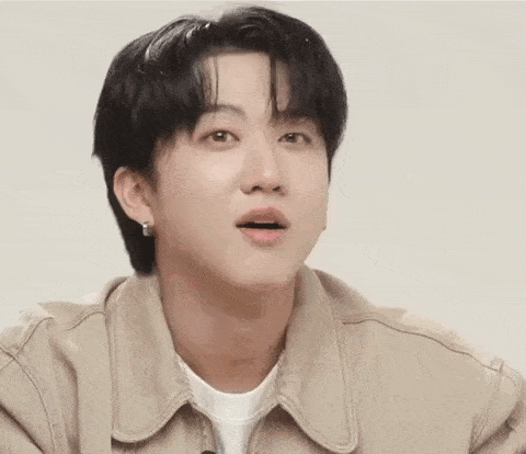 a young man wearing a tan jacket and earrings is making a surprised face .