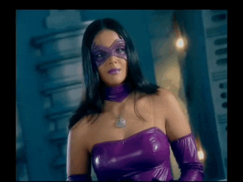a woman in a purple superhero costume and mask is standing in a dark room .