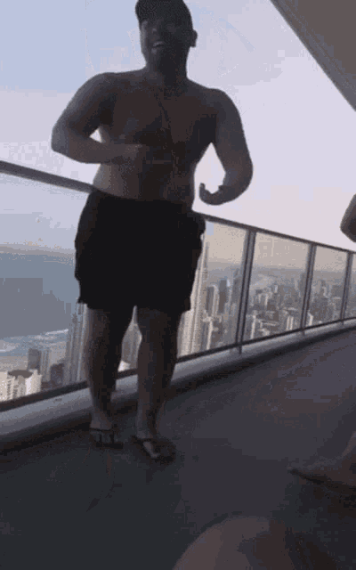 a shirtless man standing on a balcony overlooking the ocean