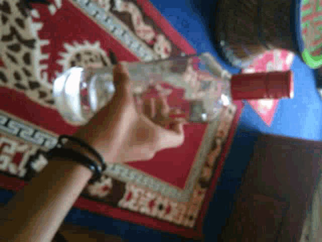 a person is holding a bottle of water in front of a rug that has the letter e on it