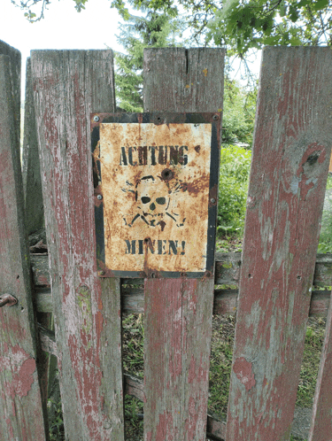 a rusty sign on a wooden fence that says achtung miners