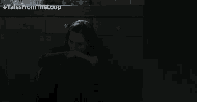 a woman sits on the floor in a dark room with #talesfromtheloop in the corner