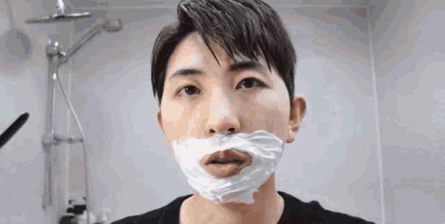 a young man is shaving his face with a razor in the bathroom .