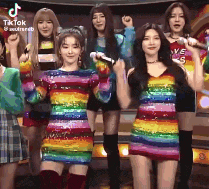 a group of girls in rainbow colored dresses are standing on a stage holding microphones .