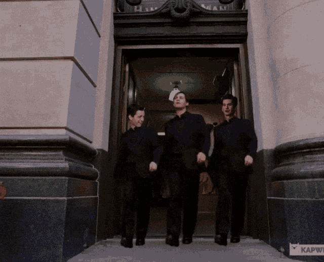 three men are walking in front of a building that says kapwi on it
