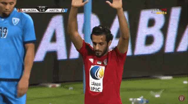 a man in a red shirt with the word ipic on it stands on a soccer field