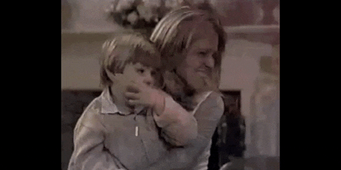 a woman is holding a young boy in her arms and the boy is covering his nose .