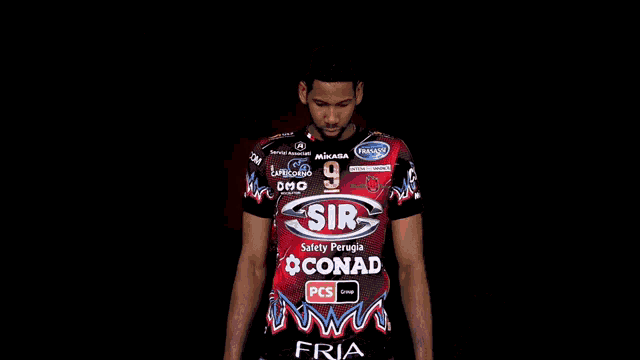 a man wearing a red and black shirt with the number 9 on it stands with his arms crossed