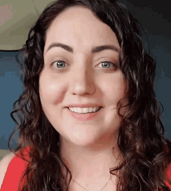 a woman with curly hair is smiling and wearing a red tank top