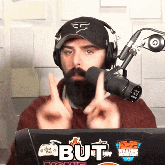 a man with a beard is giving the middle finger in front of a microphone and a laptop that says but