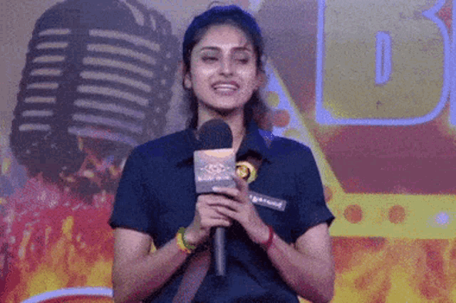 a woman is holding a microphone and smiling in front of a microphone with the letter b on it