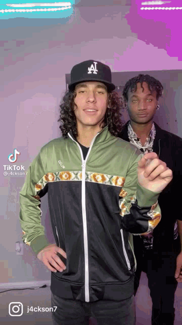 a man wearing a la hat stands next to another man wearing a jacket