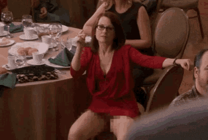 a woman in a red dress is sitting on a chair with her legs crossed at a dinner table .