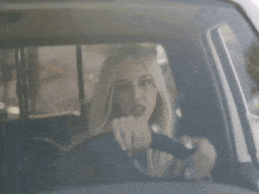a blonde woman is driving a car and looking at the camera