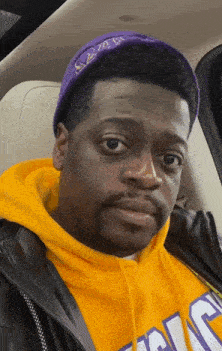 a man wearing a purple hat and a yellow hoodie has a serious look on his face