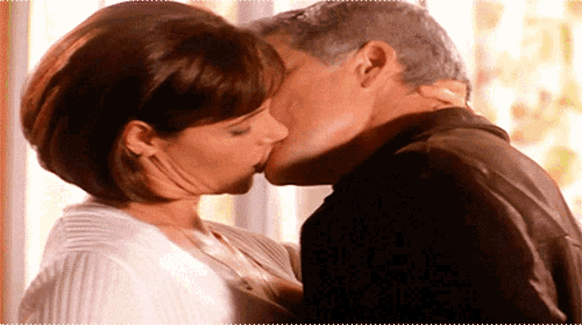 a man and a woman are kissing each other in front of a window