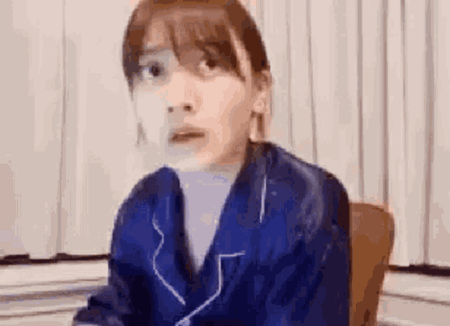 a woman in a blue pajama suit is sitting in a chair and making a surprised face .