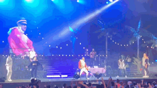a group of people are dancing on a stage with a large inflatable spongebob on the screen