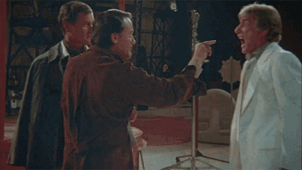 a man is screaming at another man in a movie while another man holds his hand to his face .