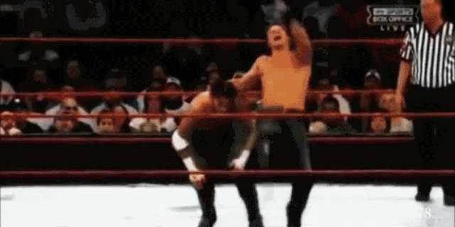 two men are wrestling in a wrestling ring with a referee standing behind them .