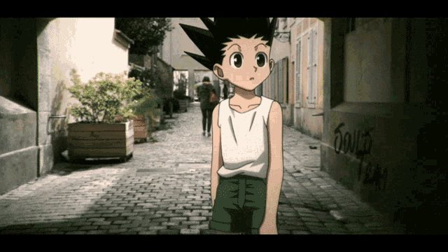 a boy in a white tank top is standing on a cobblestone street with graffiti on the side of a building that says bouge