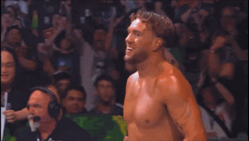 a shirtless wrestler is standing in front of a crowd with a green shirt that says ' wwe ' on it