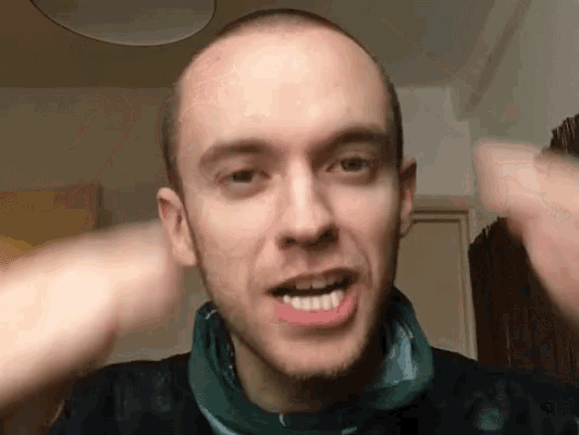 a man with a shaved head and a green scarf around his neck looks at the camera