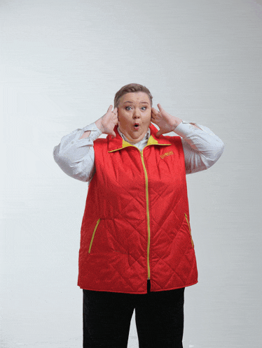 a woman wearing a red vest with a yellow zipper has her hands to her ears