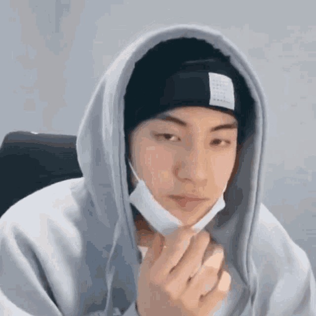 a young man wearing a hoodie and a beanie is holding his hand to his face .