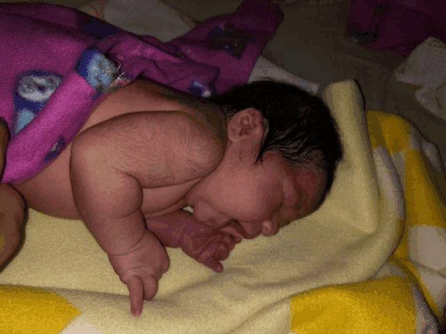 a baby is wrapped in a pink blanket and laying on a yellow blanket