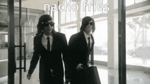 two men in suits are walking in a hallway with the word nacho fries written on the bottom