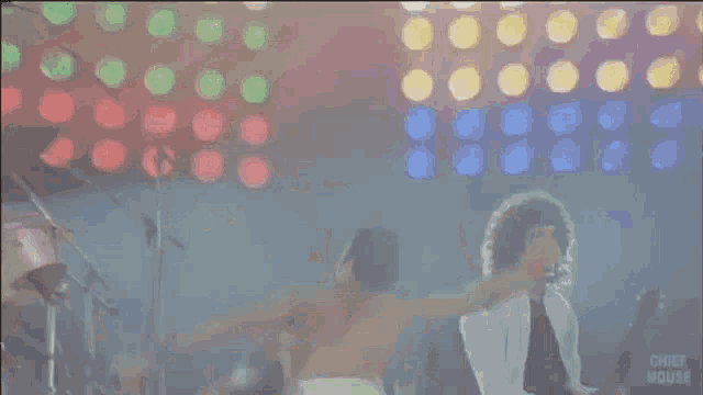 a man without a shirt is singing into a microphone on a stage