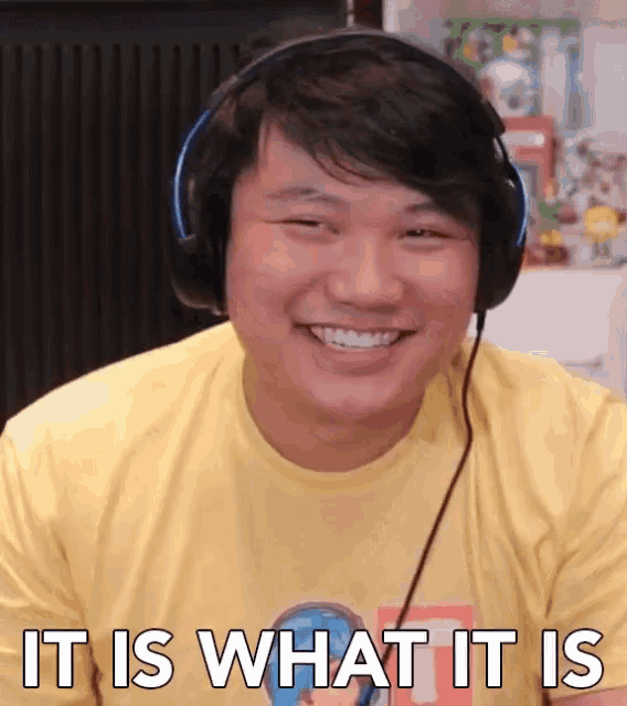 a man wearing headphones and a yellow shirt is smiling and says it is what it is