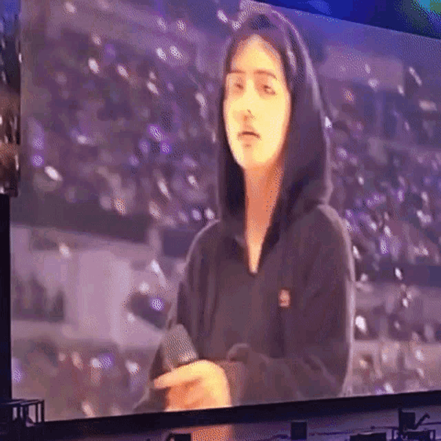 a woman in a black hoodie is holding a microphone in front of a screen .