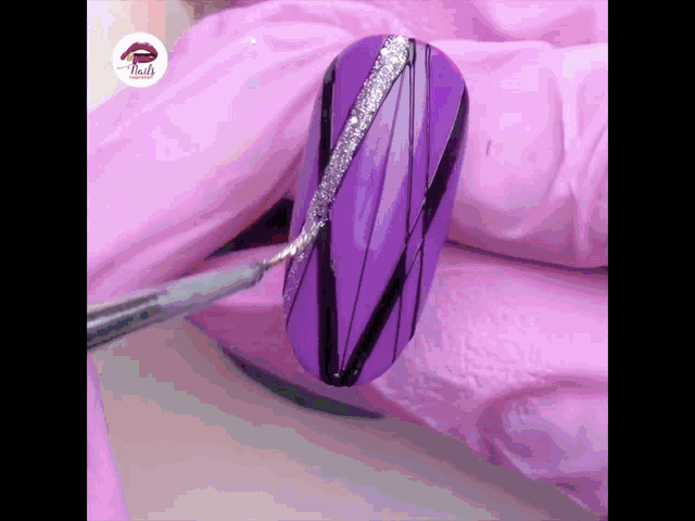 a purple nail is being painted with a black and silver design