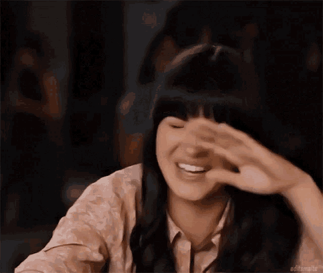 a woman with bangs is laughing with her mouth open and her hand on her face .