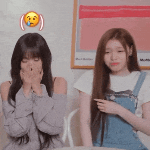 two girls are sitting next to each other with one covering her mouth with her hands