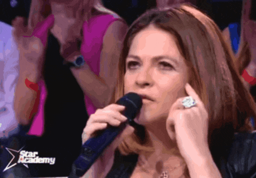 a woman singing into a microphone in front of a star academy sign