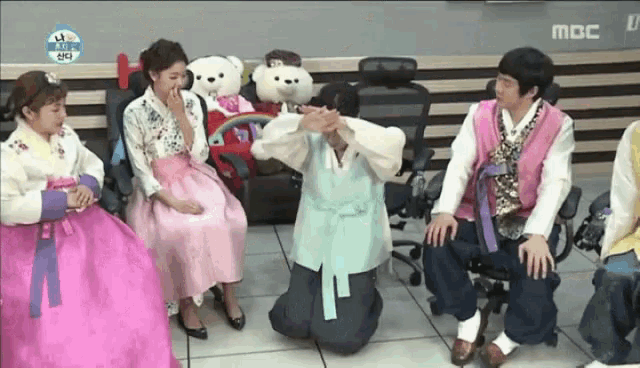 a group of people dressed in traditional korean clothing are sitting in chairs and kneeling down