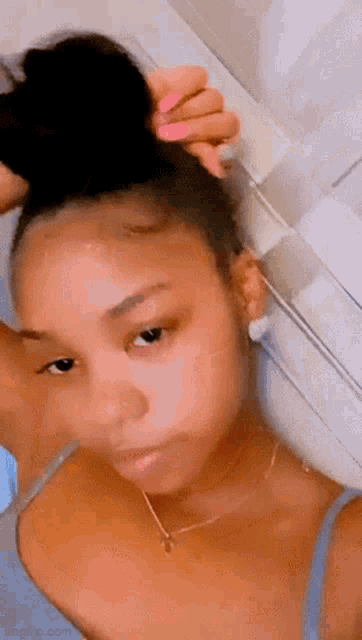 a woman is taking a selfie with her hair in a bun while wearing a necklace and earrings .