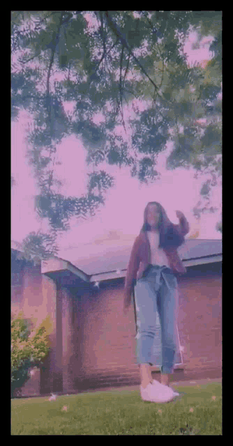 a girl is standing in the grass in front of a house